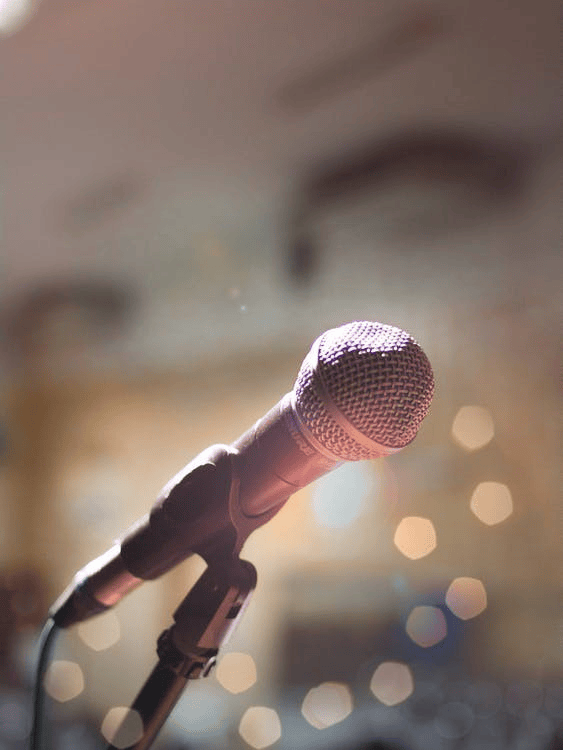 Close-up of a microphone on a stand with blurred lights in the background.
